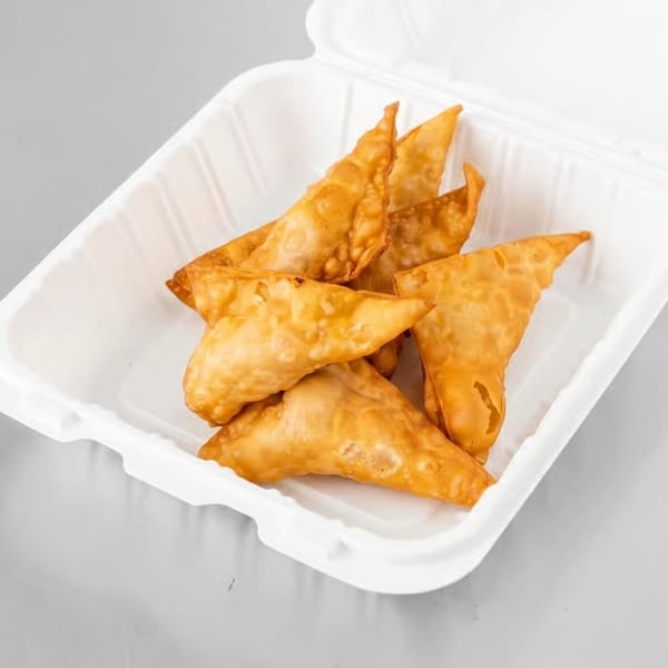 Golden-brown fried wontons in a white takeout container on a gray surface.