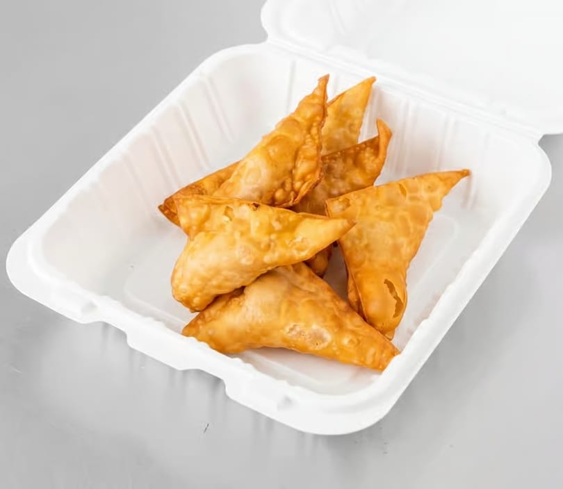 Golden-brown fried wontons in a white takeout container on a gray surface.