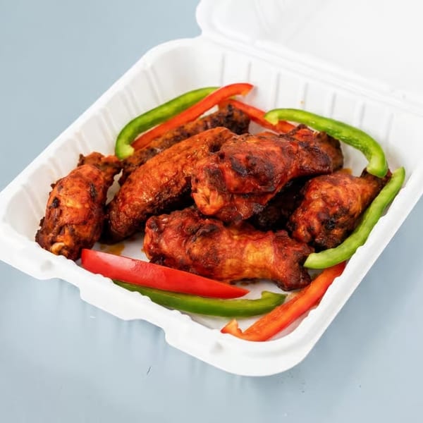 Spicy chicken wings with red and green bell pepper strips in a white takeout container.