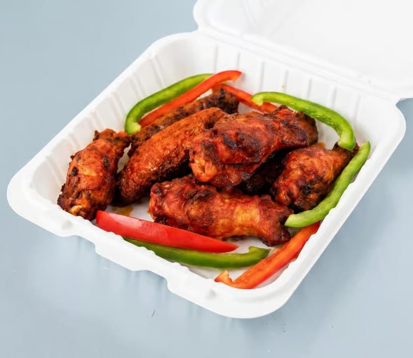 Spicy chicken wings with red and green bell pepper strips in a white takeout container.