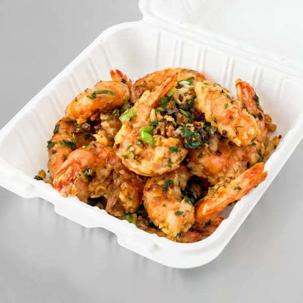 Garlic shrimp with green onions and herbs in a white takeout container.