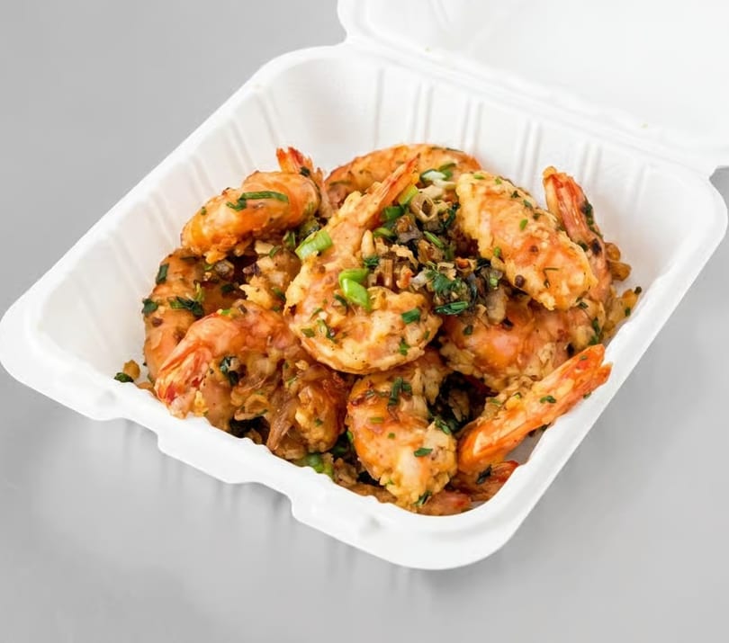 Garlic shrimp with green onions and herbs in a white takeout container.