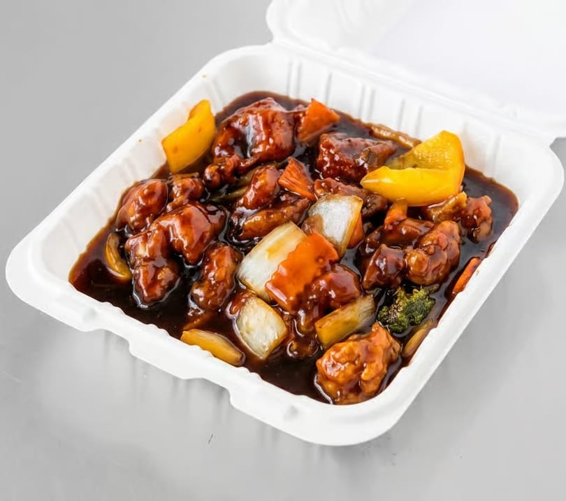 Sweet and sour chicken with bell peppers and onions in a white takeout container.